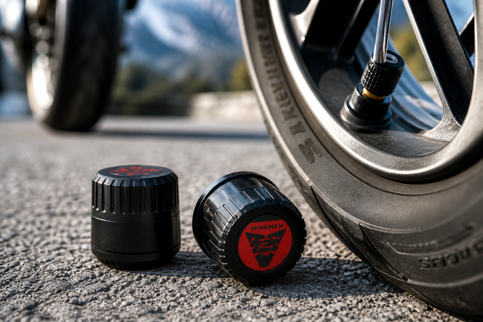 Motul Ride TPMS Sensors – Motorcycle Tire Pressure Monitoring Motorcycle tire pressure sensors placed on asphalt next to a wheel in a mountain environment